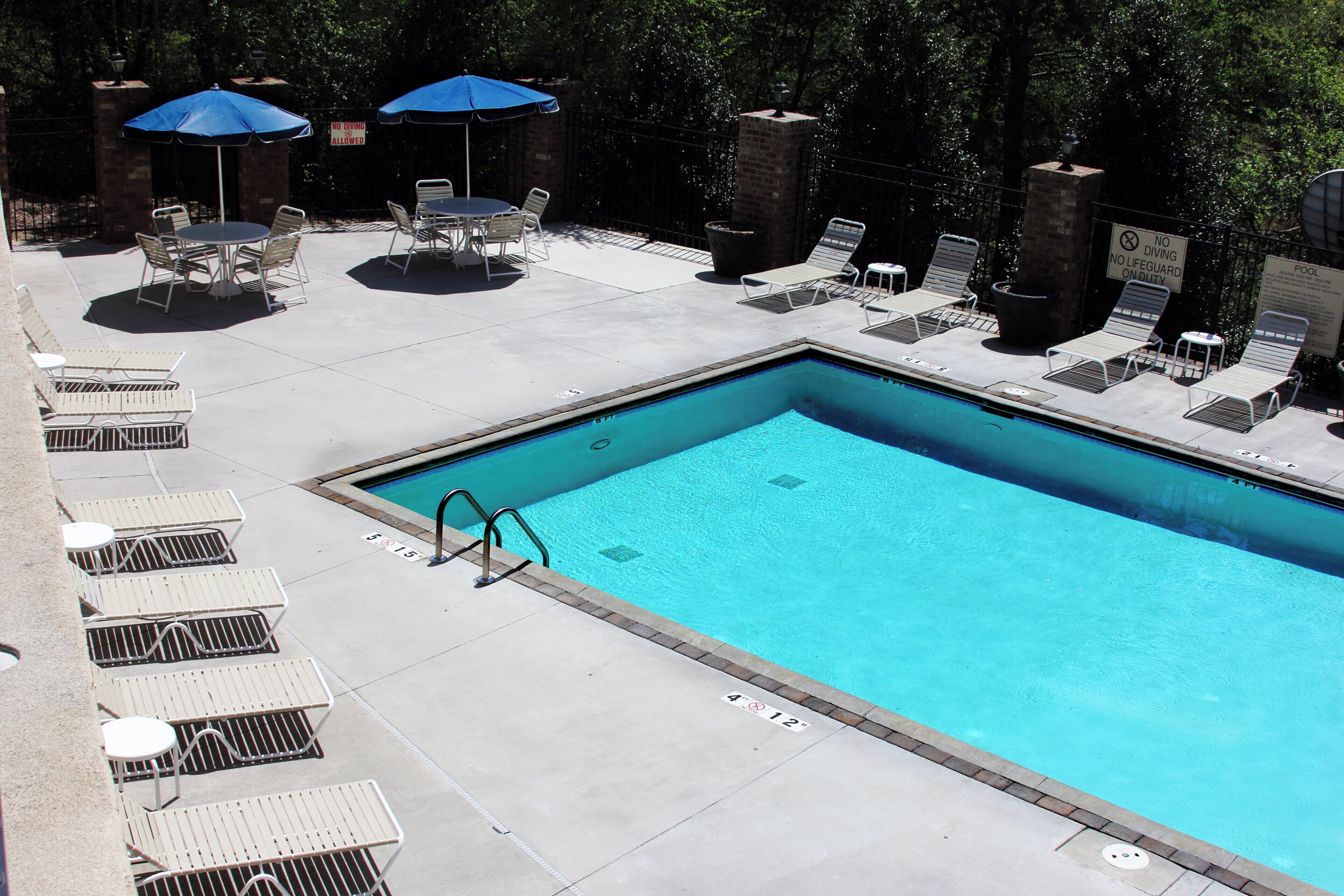A rectangular swimming pool with a diving board, surrounded by lounge chairs and umbrellas.