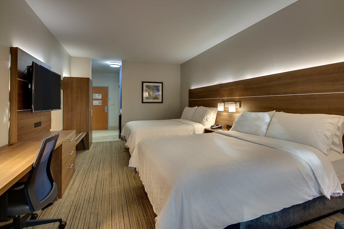 Ett hotellrum med två sängar, ett skrivbord med en stol, en platt-TV och en sänggavel i trä.