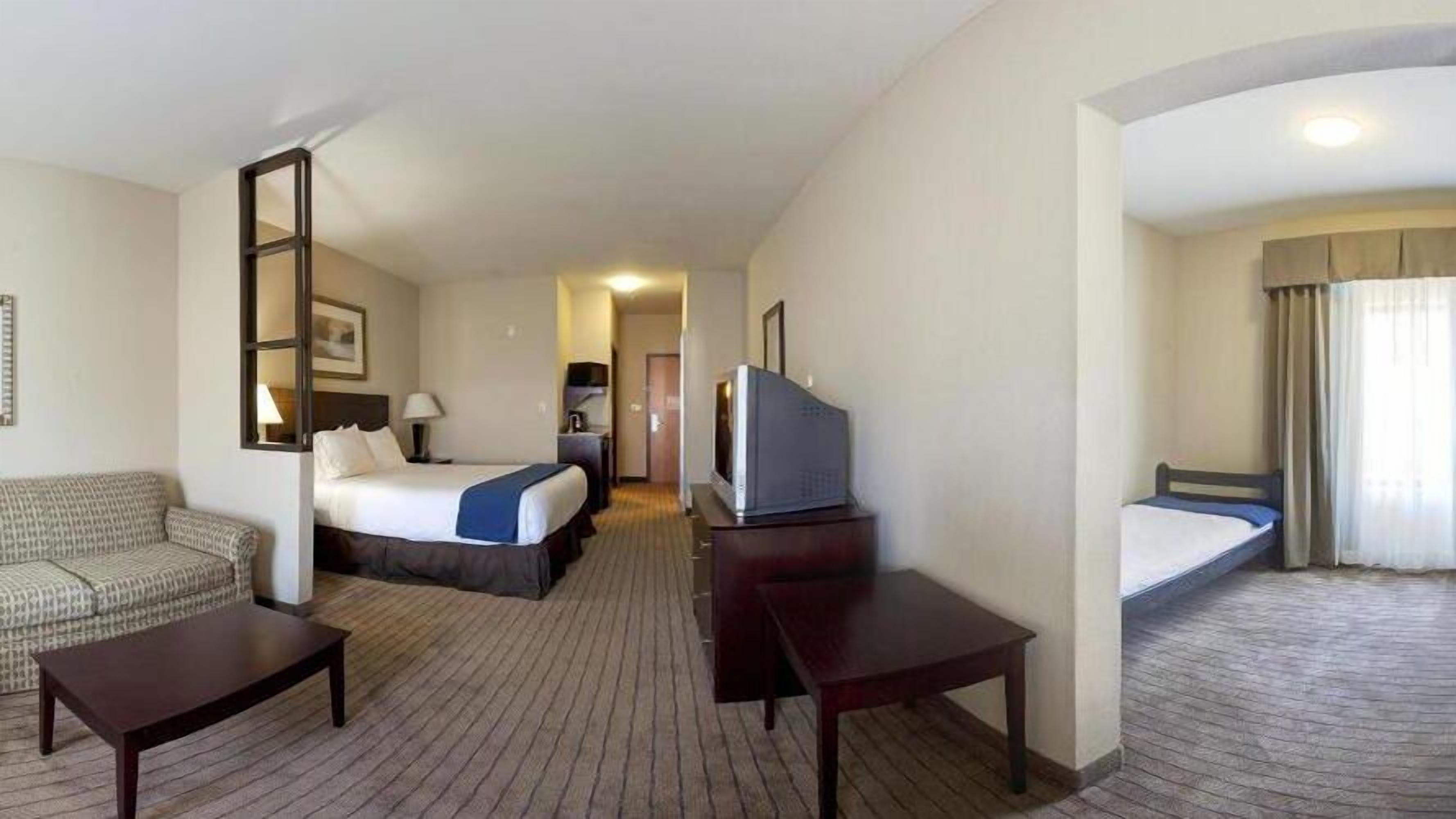 Habitación de hotel con sofá, cama, escritorio, televisión y una pequeña mesa.