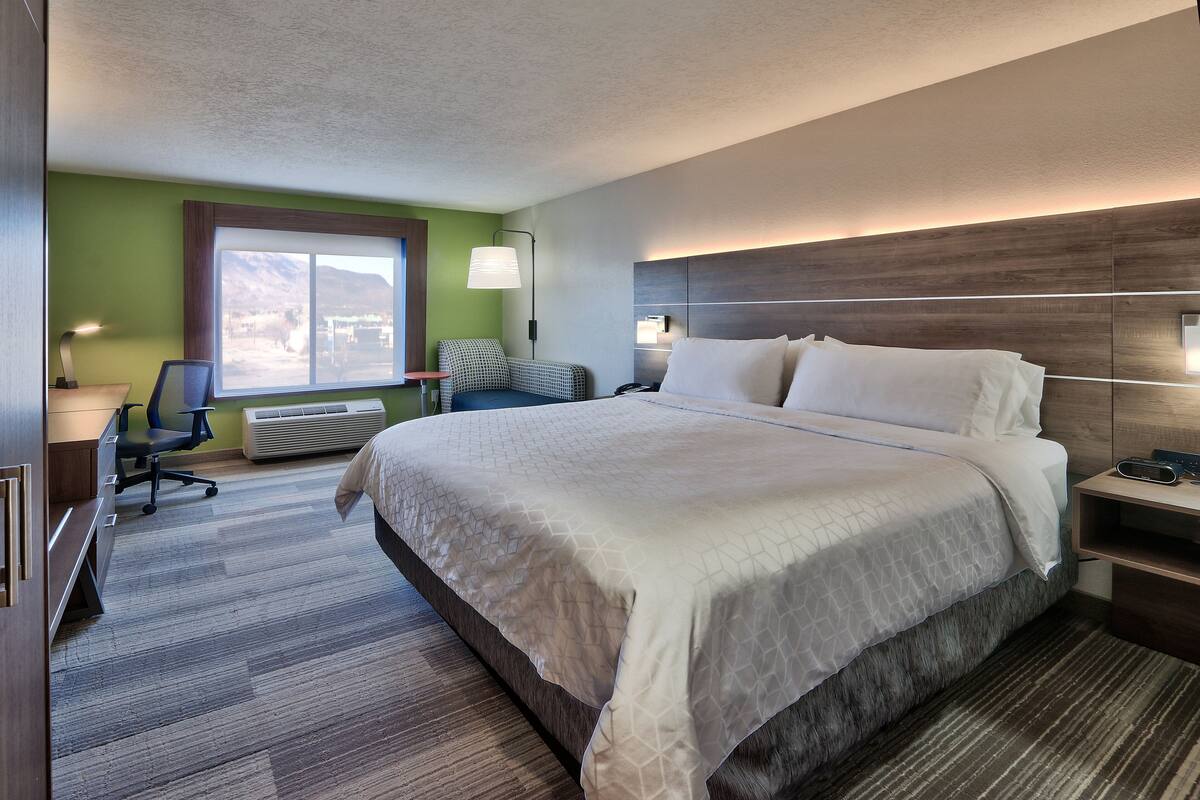 Ein Hotelzimmer mit einem großen Bett, einem Schreibtisch, einem Stuhl, einer Lampe und einem Fenster mit Blick auf die Berge.