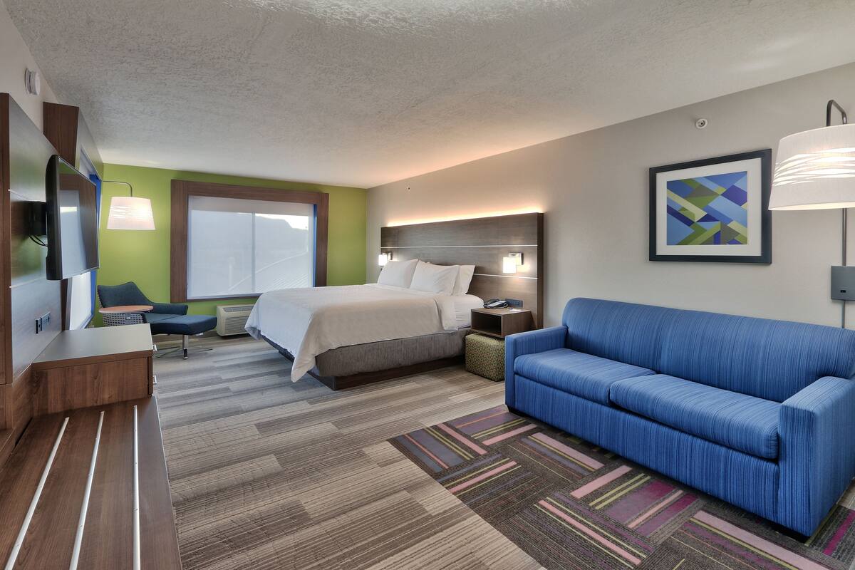 Ein Hotelzimmer mit einem Bett, einem blauen Sofa, einem Fernseher und einem Schreibtisch.