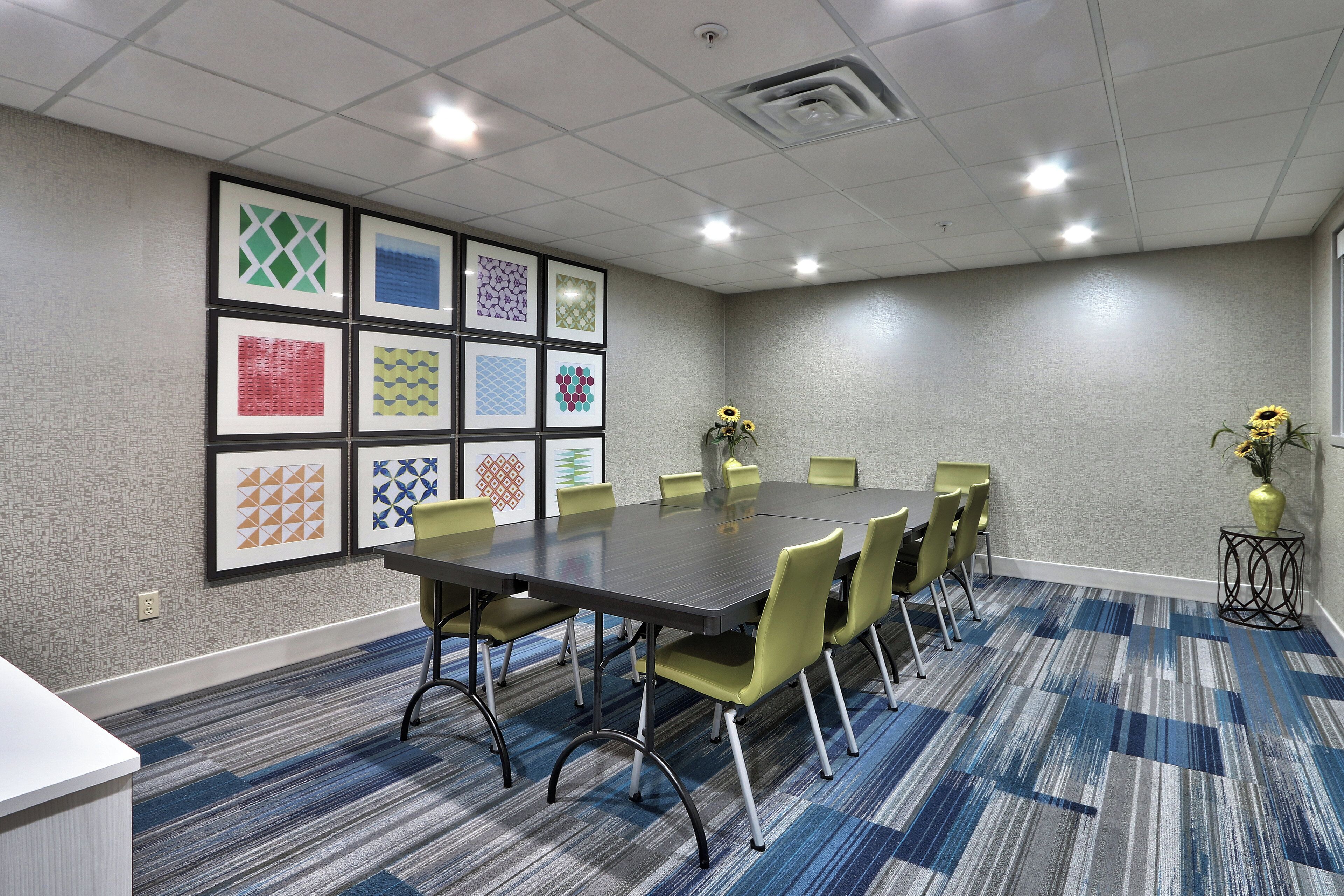 A conference room with a long table, chairs, framed artwork on the wall, and a carpeted floor.