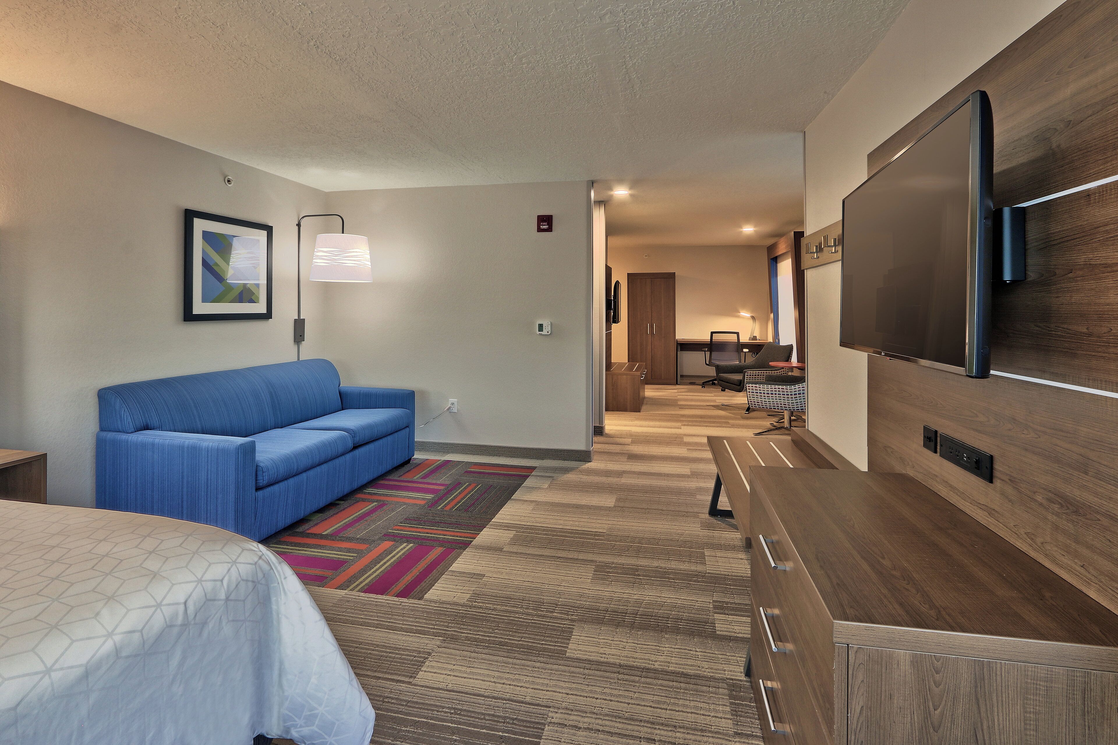 A hotel room with a blue sofa, a bed, a TV, and a desk.