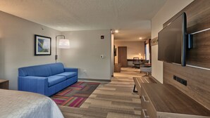 A hotel room with a bed, a blue sofa, a TV, and a desk with drawers. - Holiday Inn Express Socorro by IHG (Socorro)