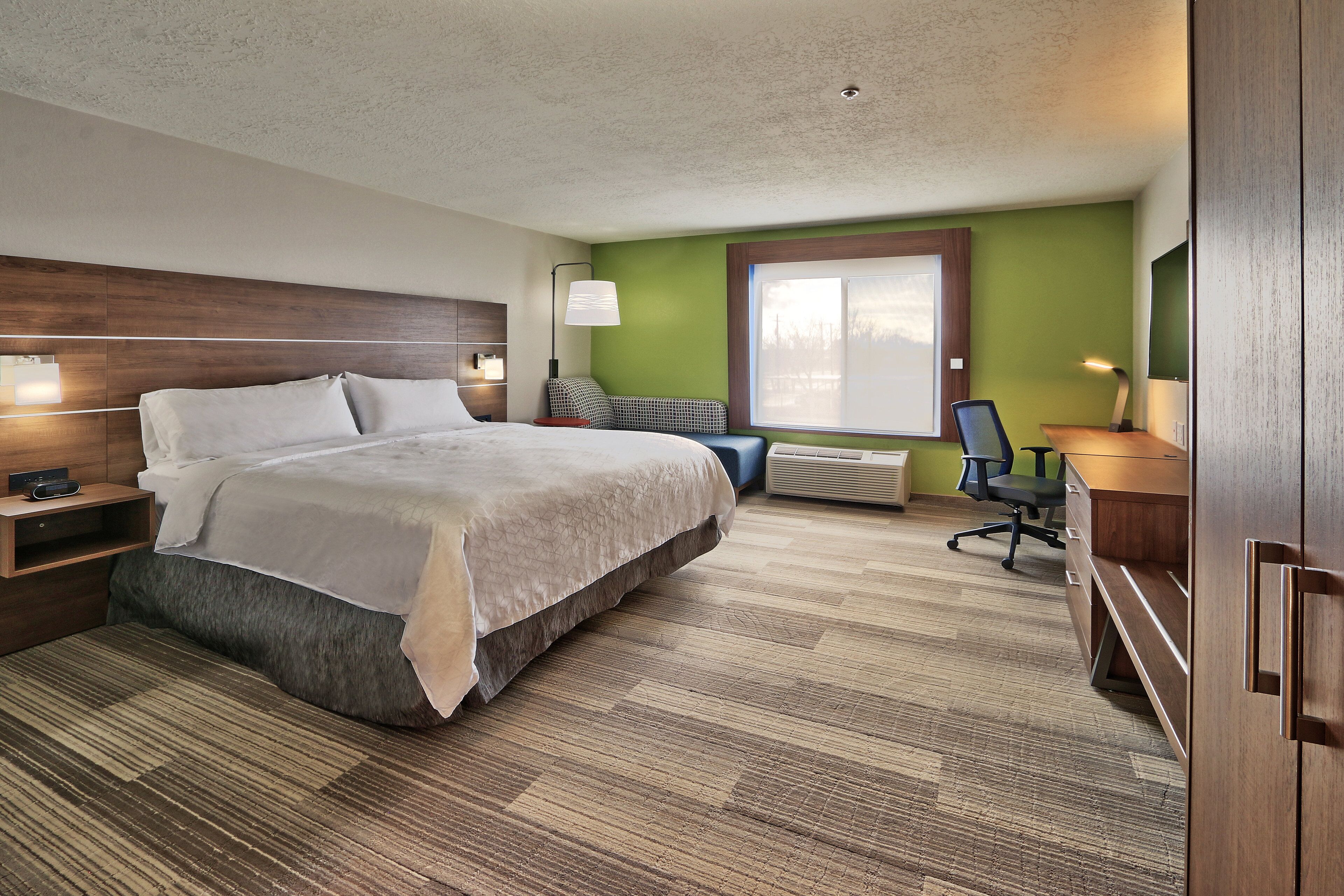 A hotel room with a large bed, a desk, a chair, a lamp, and a window.