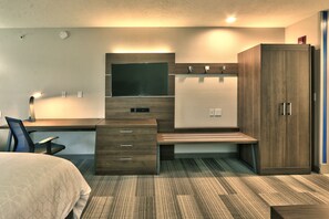 Una habitación de hotel moderna con cama, escritorio, silla, armario y televisor de pantalla plana.