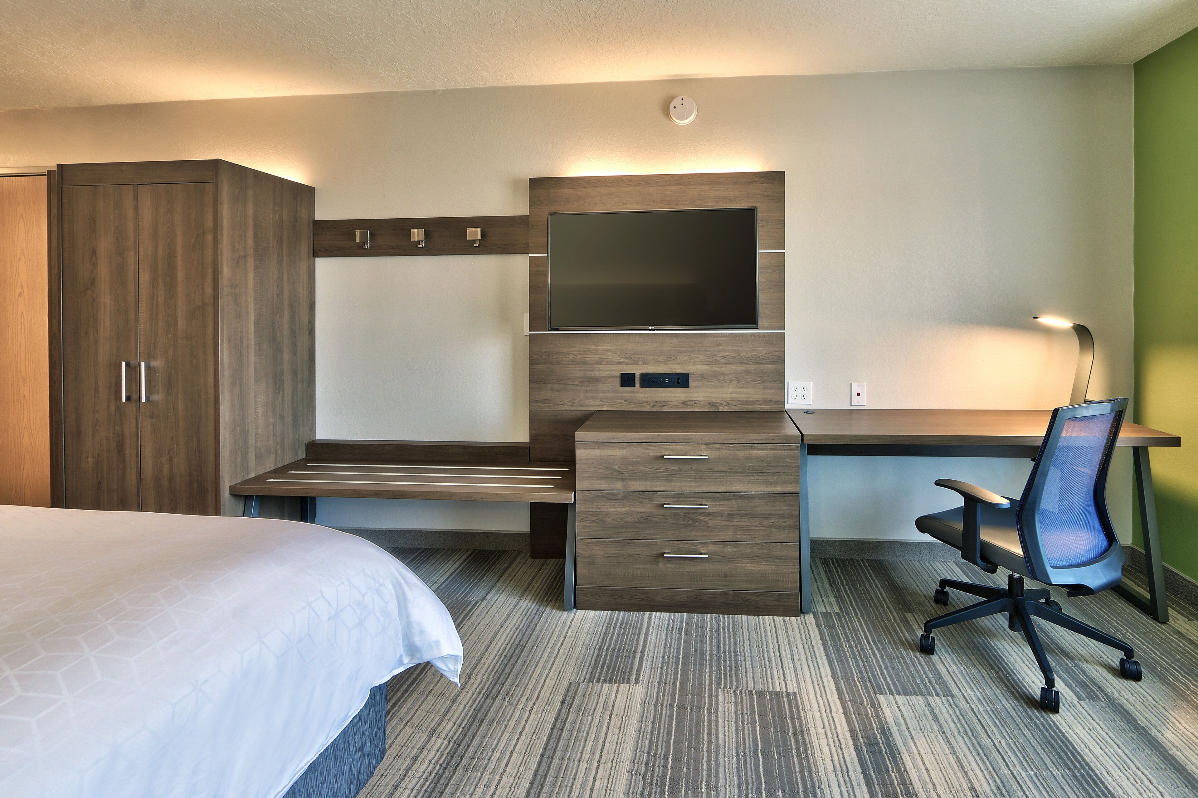 Ein Hotelzimmer mit Bett, Schreibtisch mit Fernseher, Sessel und Kleiderschrank.