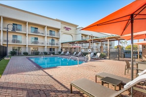A hotel with a swimming pool, outdoor seating, and a covered patio area.