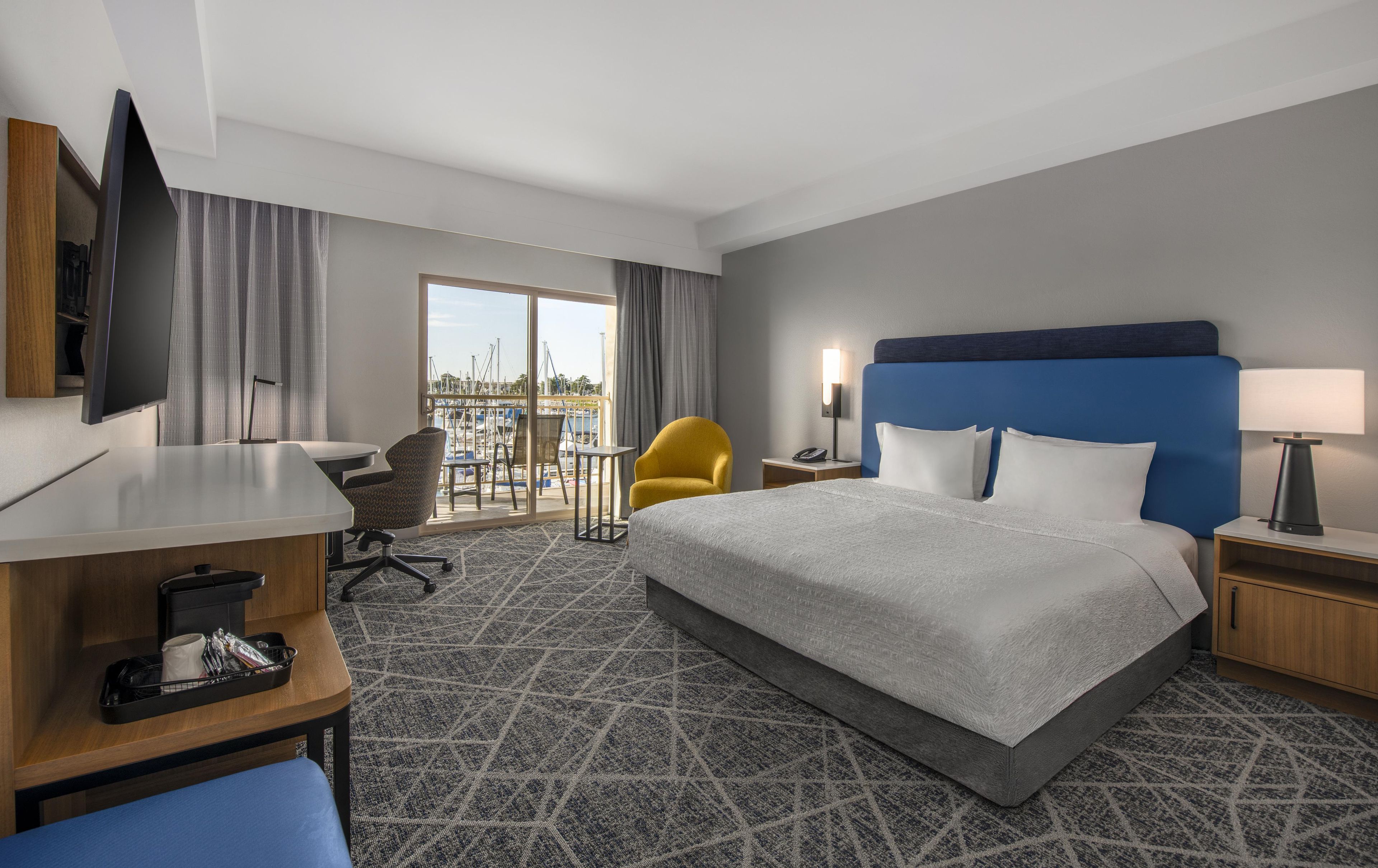 A hotel room with a bed, desk, chair, and a view of the marina.