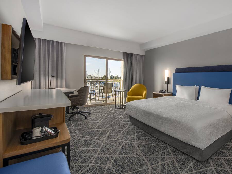 A hotel room with a bed, desk, chair, and a view of the marina.
