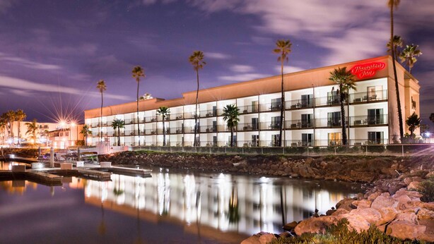 A multi-story hotel with a pool in the foreground, palm trees, and a clear night sky. - Hampton Inn Channel Islands Harbor/Oxnard (Oxnard)