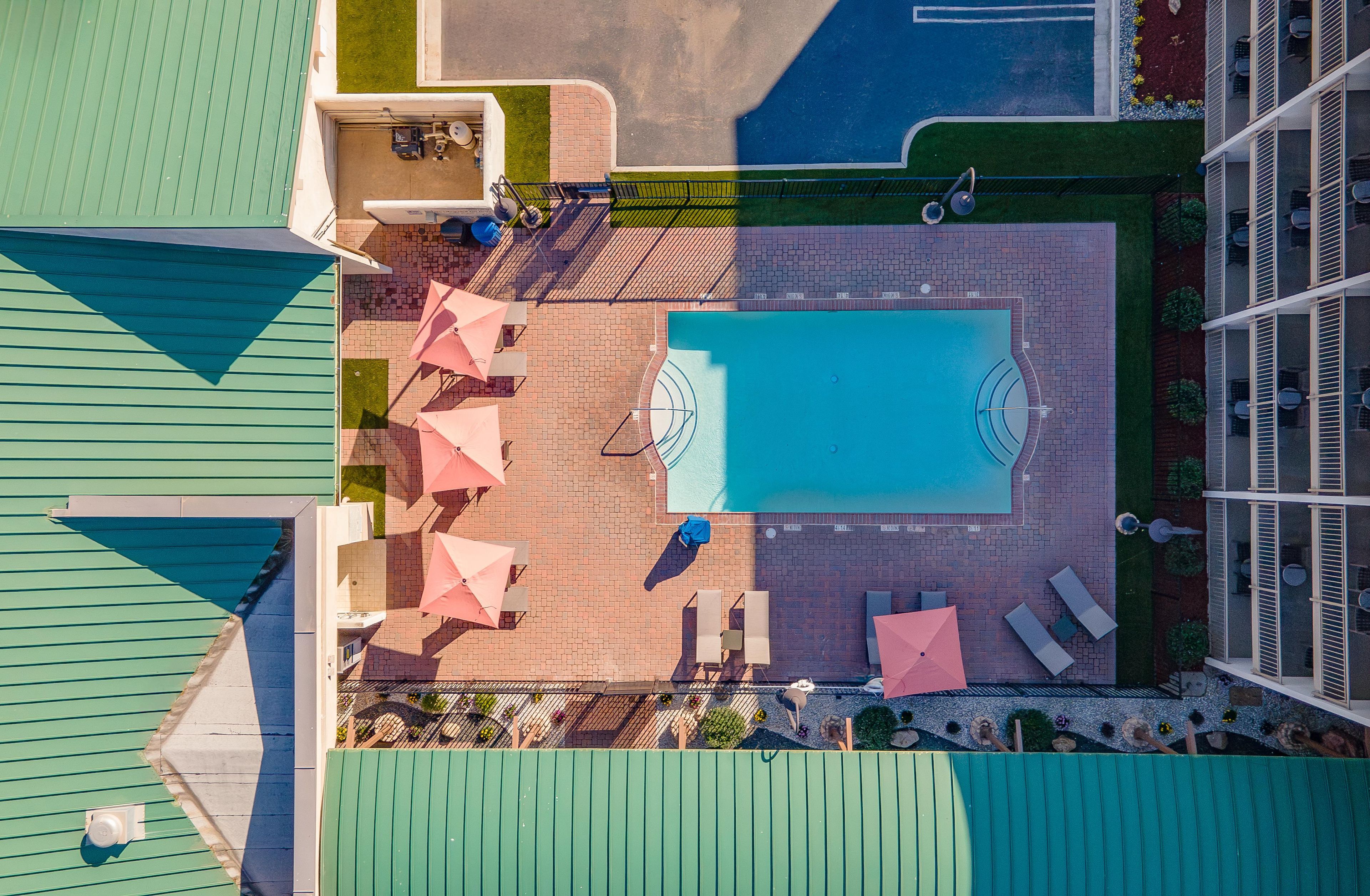 Vista aérea de uma área de piscina no terraço, com uma piscina retangular, rodeada por espreguiçadeiras e guarda-sóis.