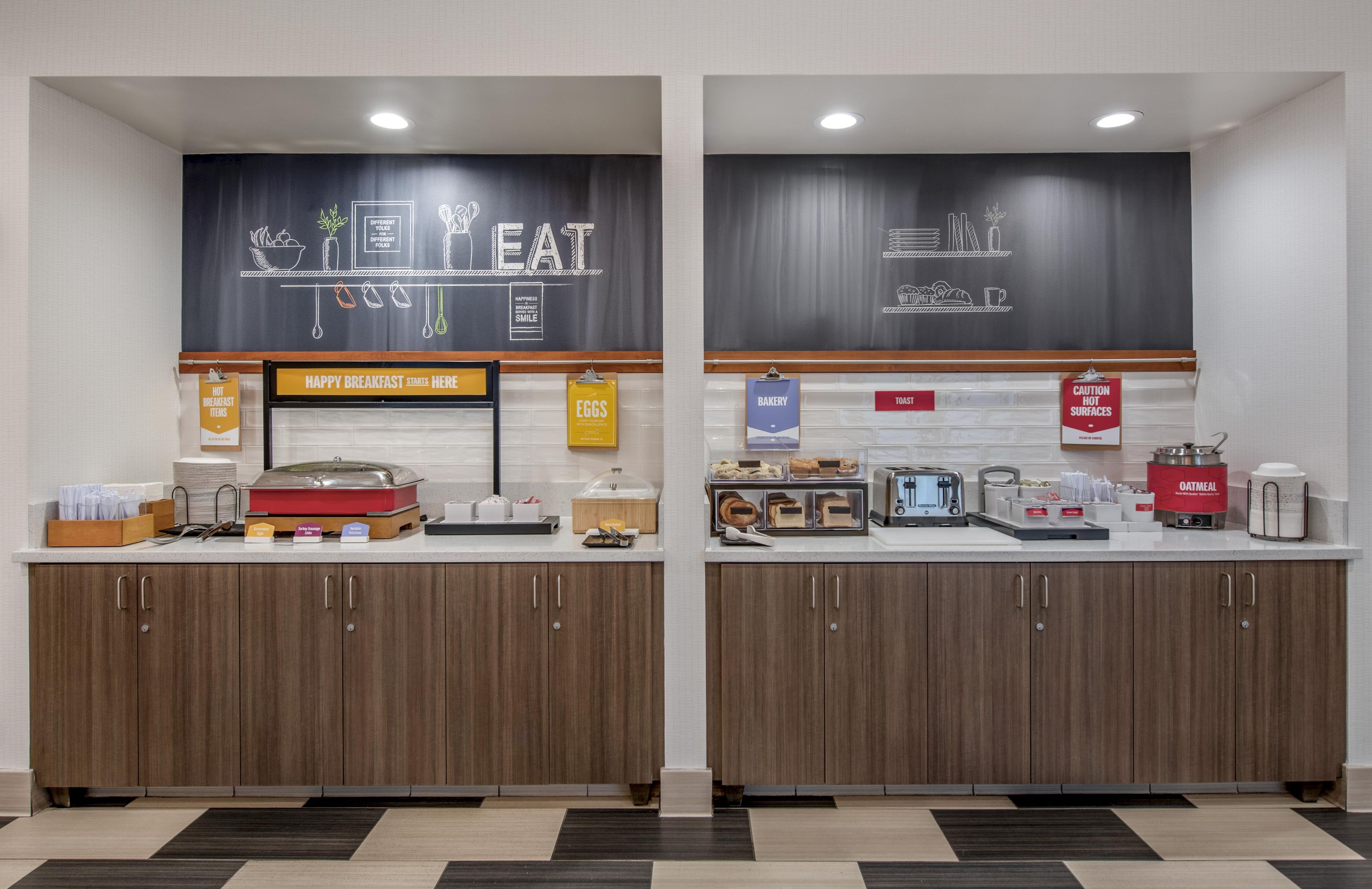 A breakfast area with a chalkboard menu, labeled sections for hot breakfast items, eggs, bakery, toast, and caution for hot surfaces.