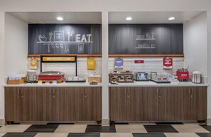 A breakfast area with a chalkboard menu, labeled sections for hot breakfast items, eggs, bakery, toast, and caution for hot surfaces. - Hampton Inn Channel Islands Harbor/Oxnard (Oxnard)