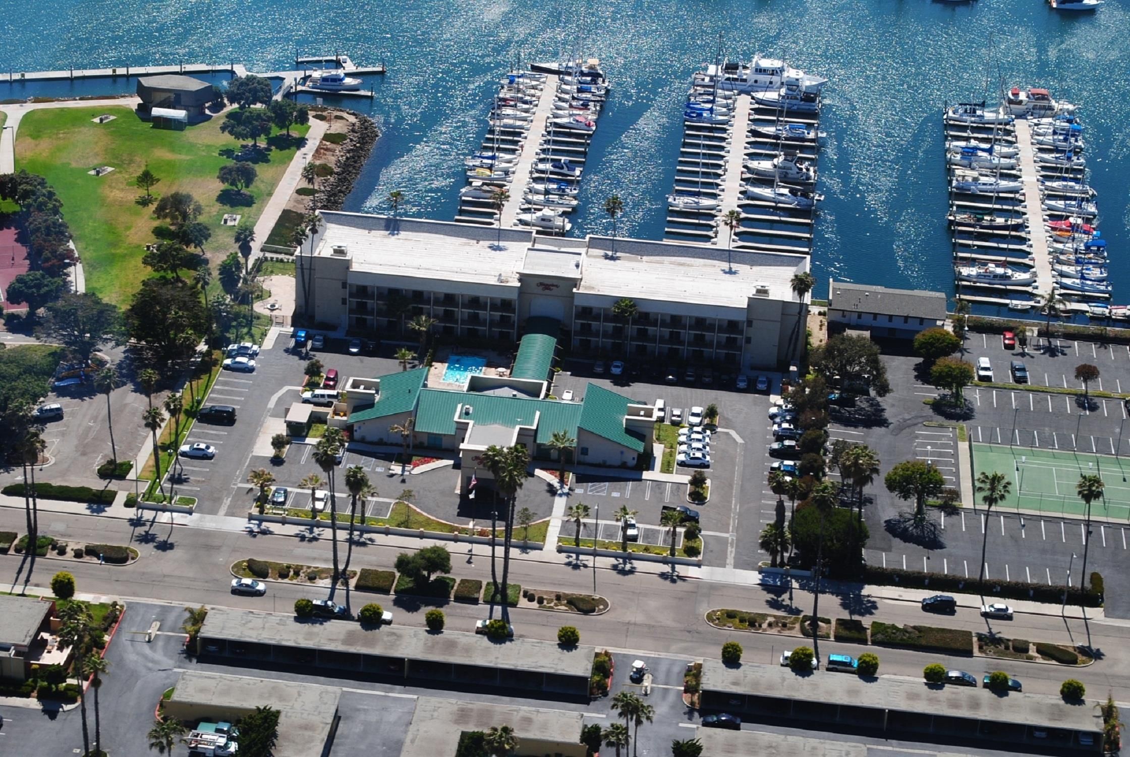 An aerial view of a marina with multiple docks and boats, a parking lot, and a building with a green roof.