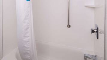 Un espace douche équipé d’un rideau de douche blanc, d’une barre d’appui et d’un pommeau de douche à main.