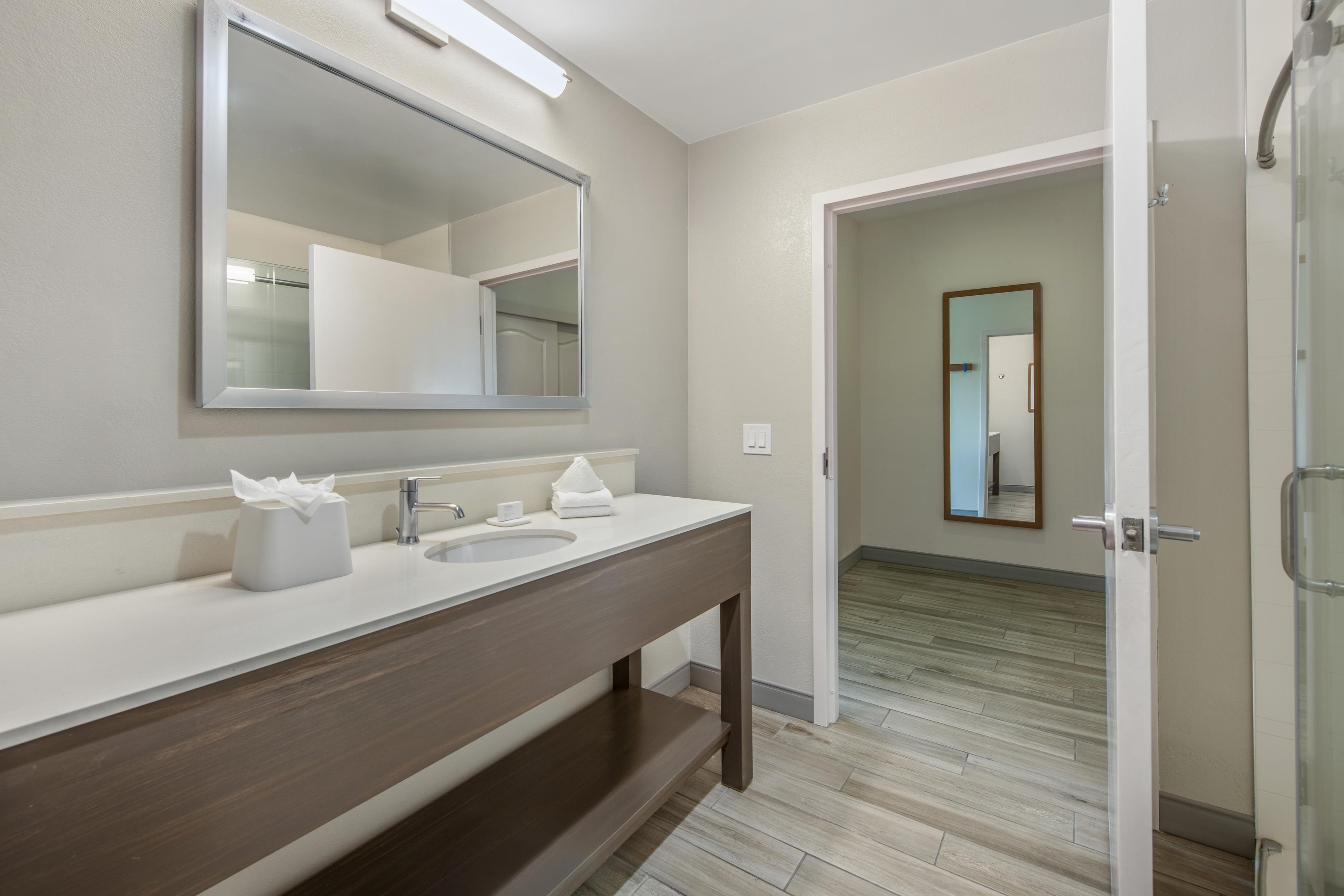 A modern bathroom with a large mirror, two sinks, and a wooden vanity.