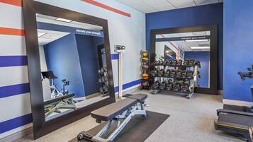 Un gimnasio con equipo de ejercicio, espejos y adhesivos motivacionales en la pared.