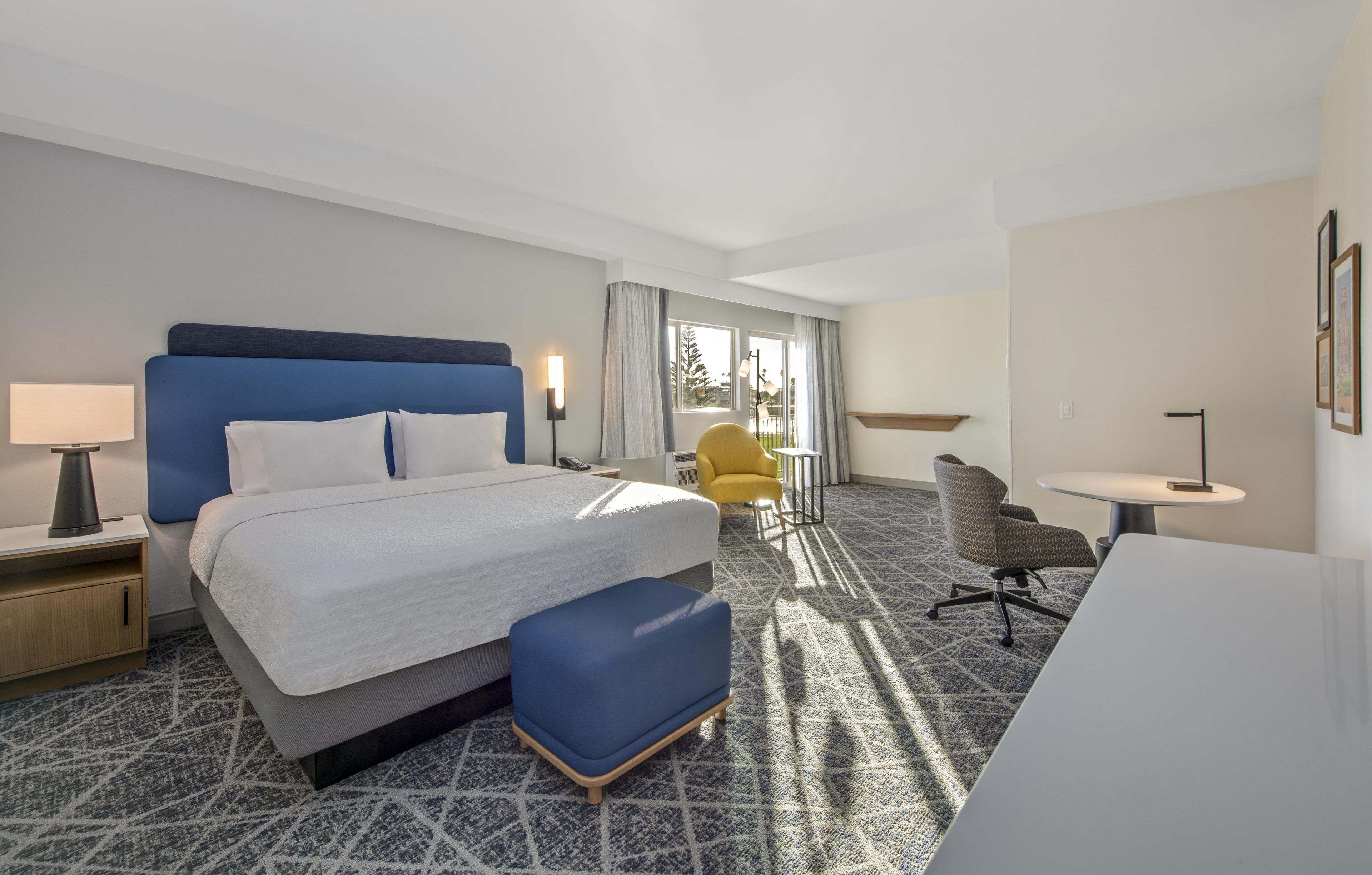 A hotel room with a large bed, a desk, a chair, and a small table.