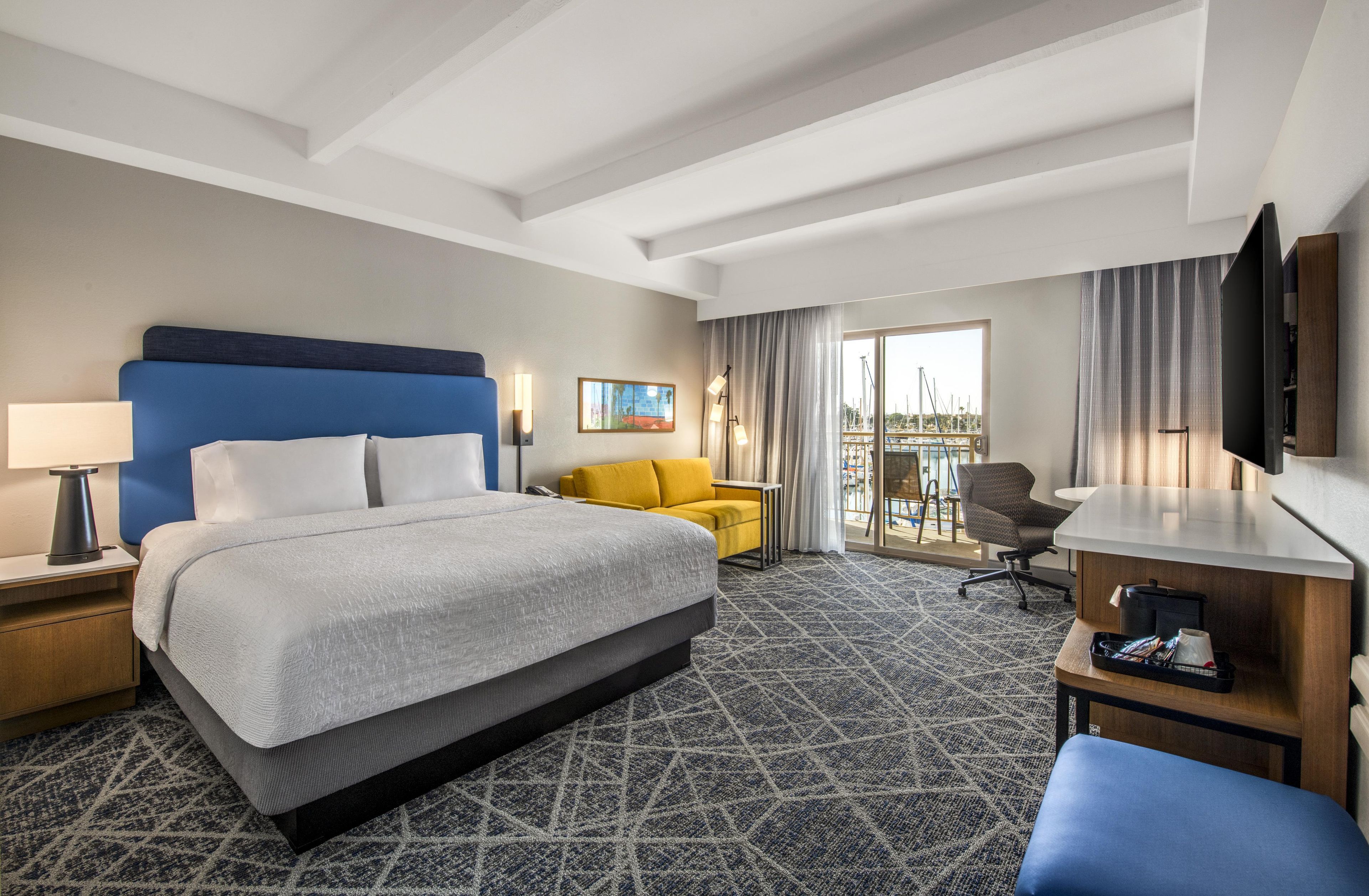 A hotel room with a large bed, a desk, a chair, and a TV.