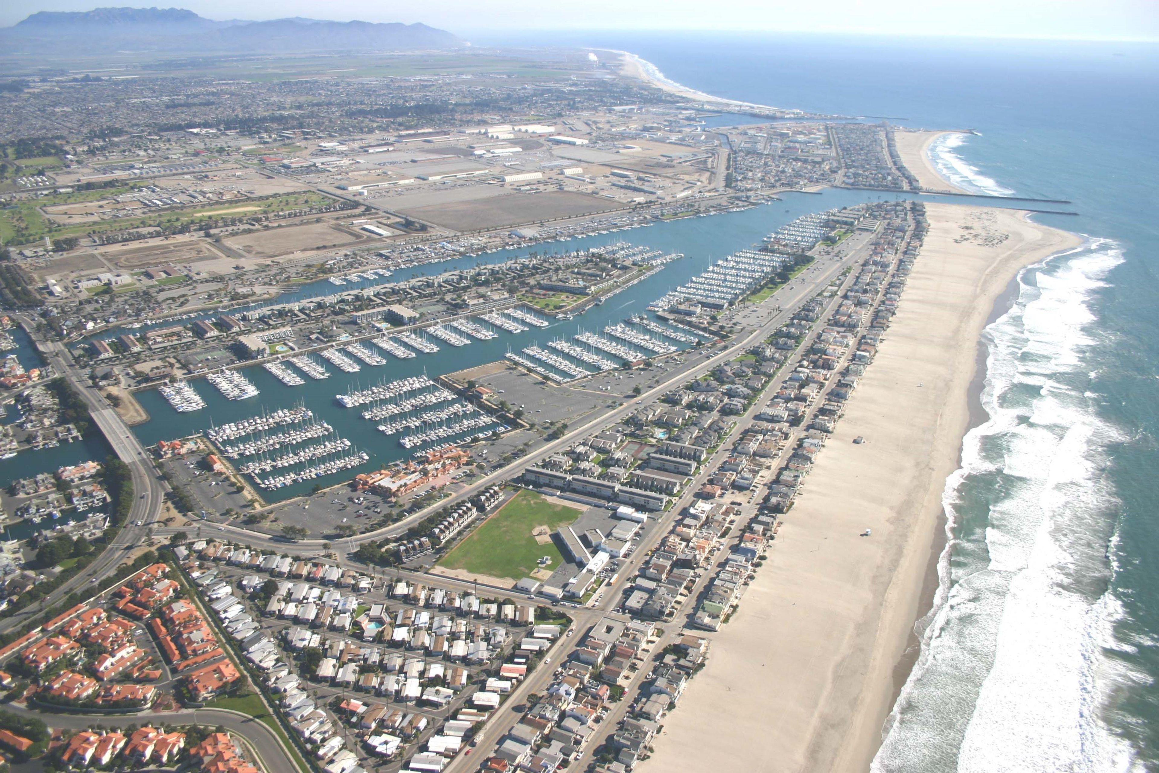 Vista aérea de una ciudad costera con un puerto deportivo, zonas residenciales y una playa.