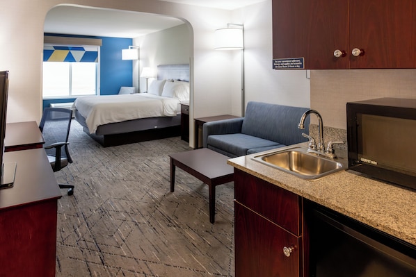 Quarto de hotel com cama, sofá, escrivaninha, pia e micro-ondas.