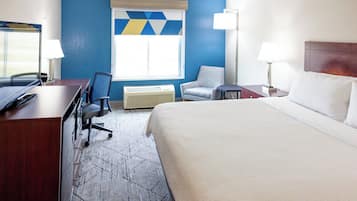 A hotel room with a large bed, a desk with a computer, a chair, a window with blinds, and a wall with a geometric pattern.