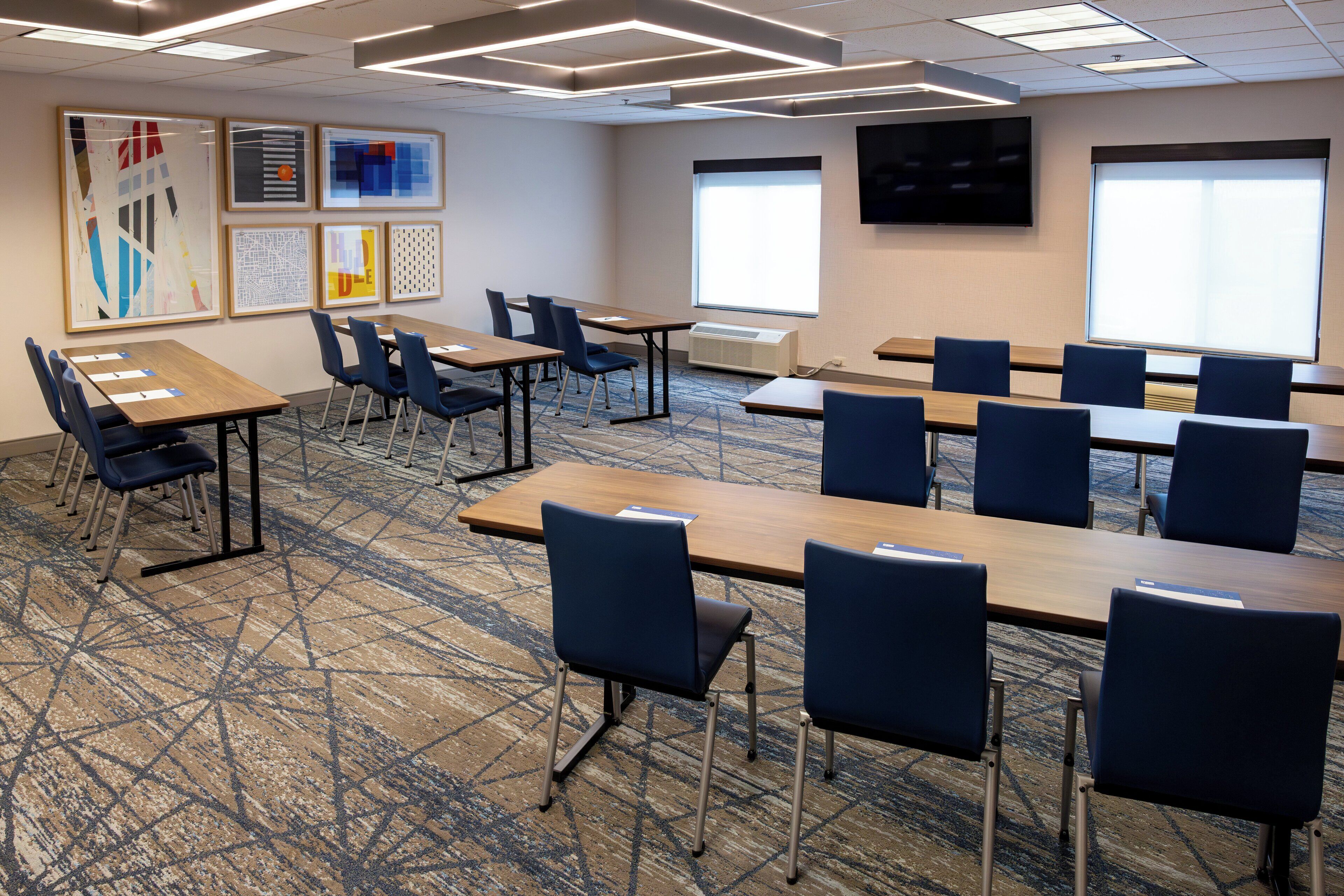 A conference room with multiple tables and chairs, large windows, and artwork on the walls.