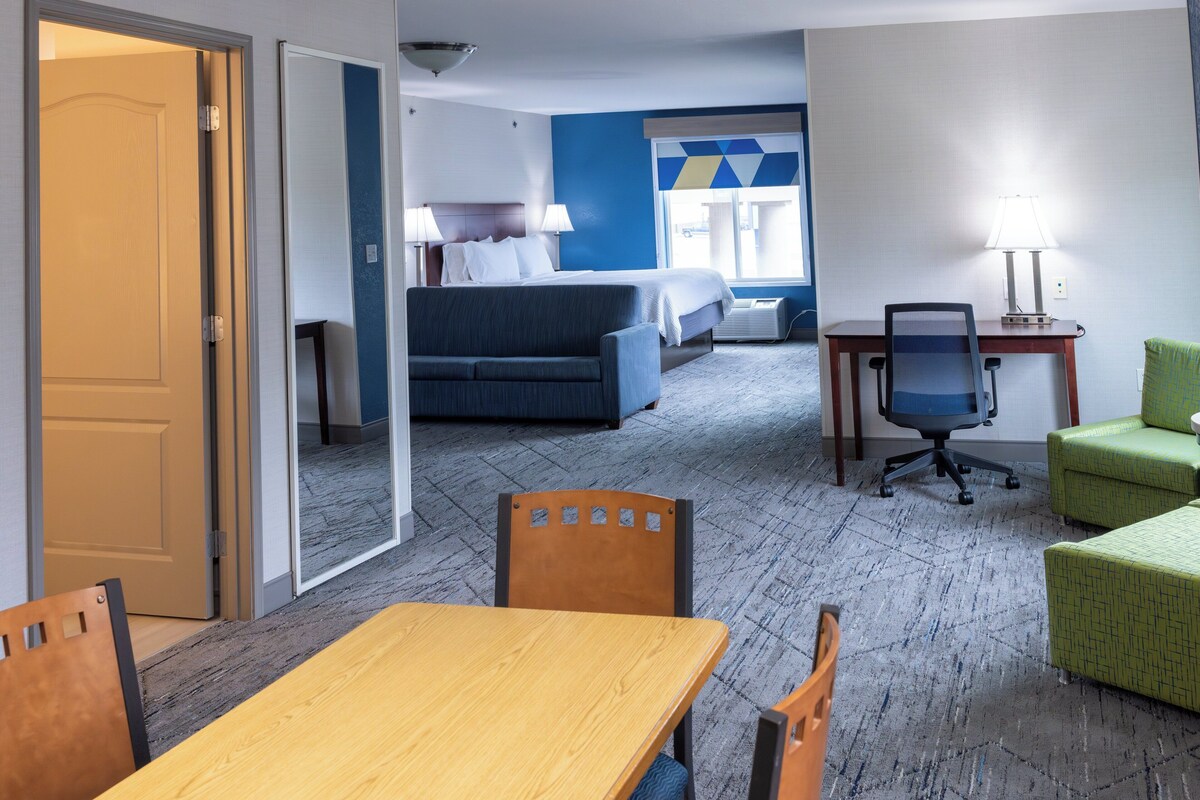 A hotel room with a bed, a desk, a chair, a table, and a green armchair.