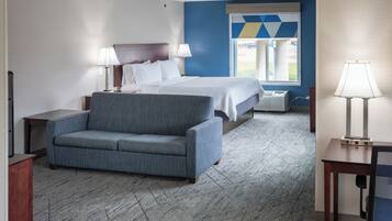 A hotel room with a bed, a sofa, a desk, and a window with a geometric view.