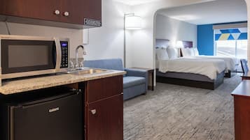A compact hotel room with a kitchenette, a bed, a sofa, and a view of the outside.