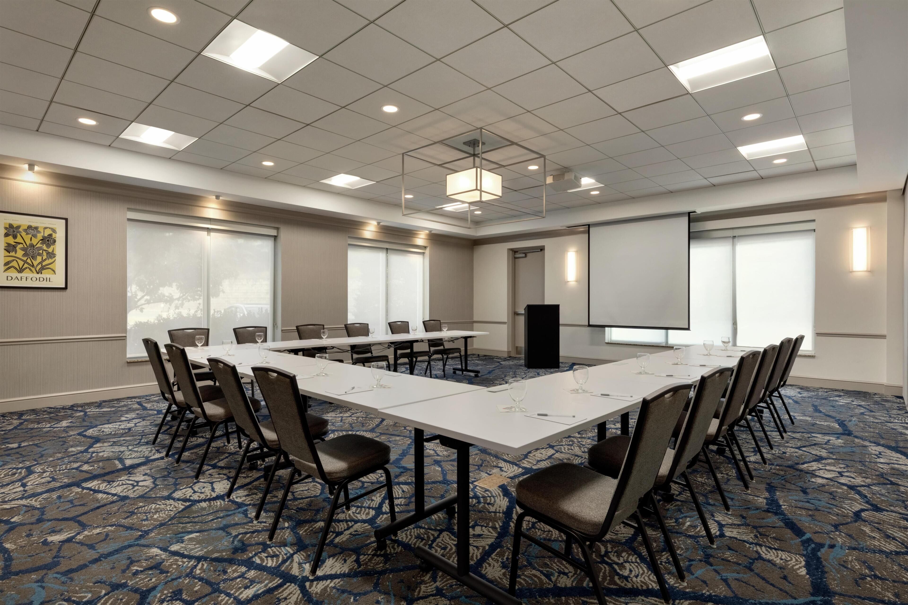 A conference room with a long table, chairs, a projector screen, and a carpeted floor.