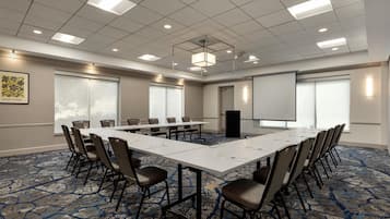 Un salón de conferencias con una larga mesa, sillas, una pantalla de proyector y piso alfombrado.