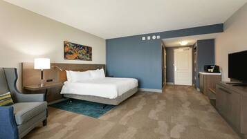 A hotel room with a bed, a desk, a chair, a TV, and a painting on the wall.