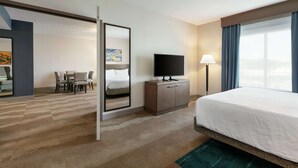 A hotel room with a bed, a television on a wooden cabinet, a desk with chairs, a mirror, and a window with curtains. - Hilton Garden Inn Harrisburg East (Harrisburg)