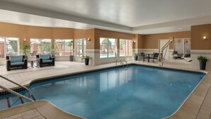 An indoor swimming pool with lounge chairs and tables, large windows, and a staircase leading to an upper level. - Hilton Garden Inn Harrisburg East (Harrisburg)