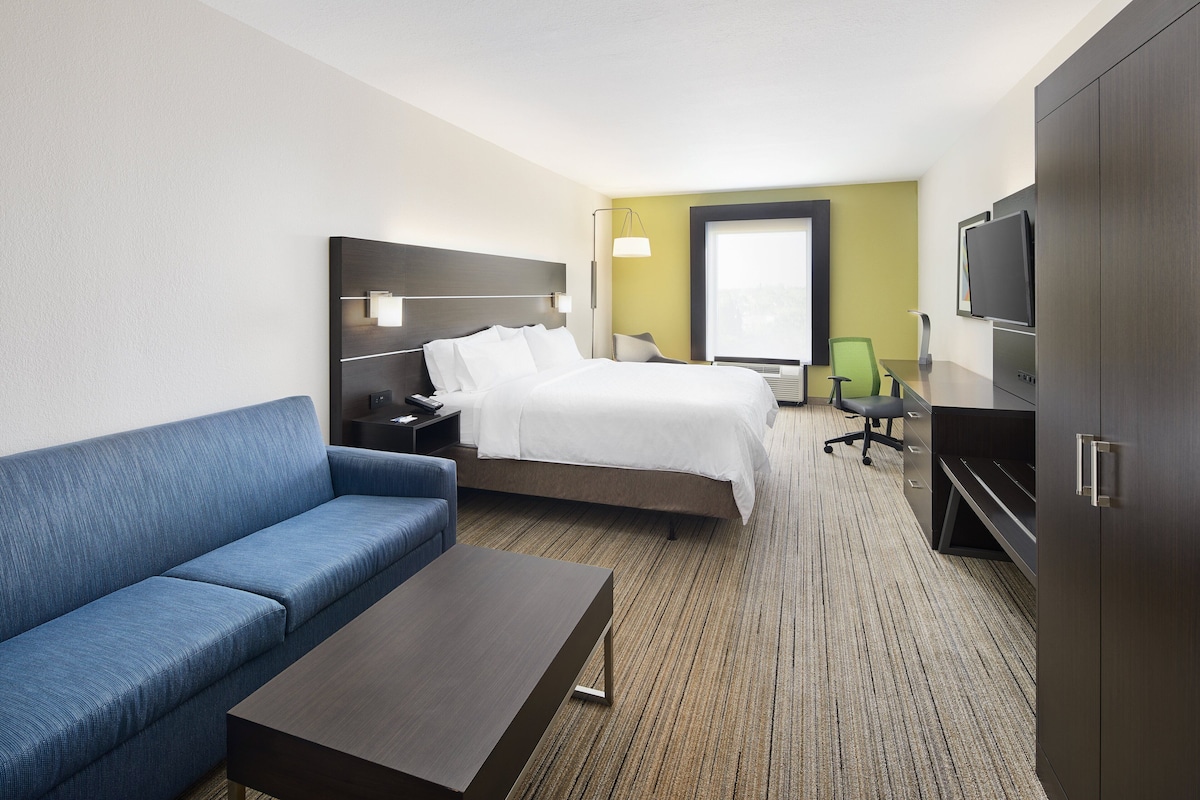Quarto de hotel com uma cama, um sofá azul, uma escrivaninha, uma televisão e uma janela.