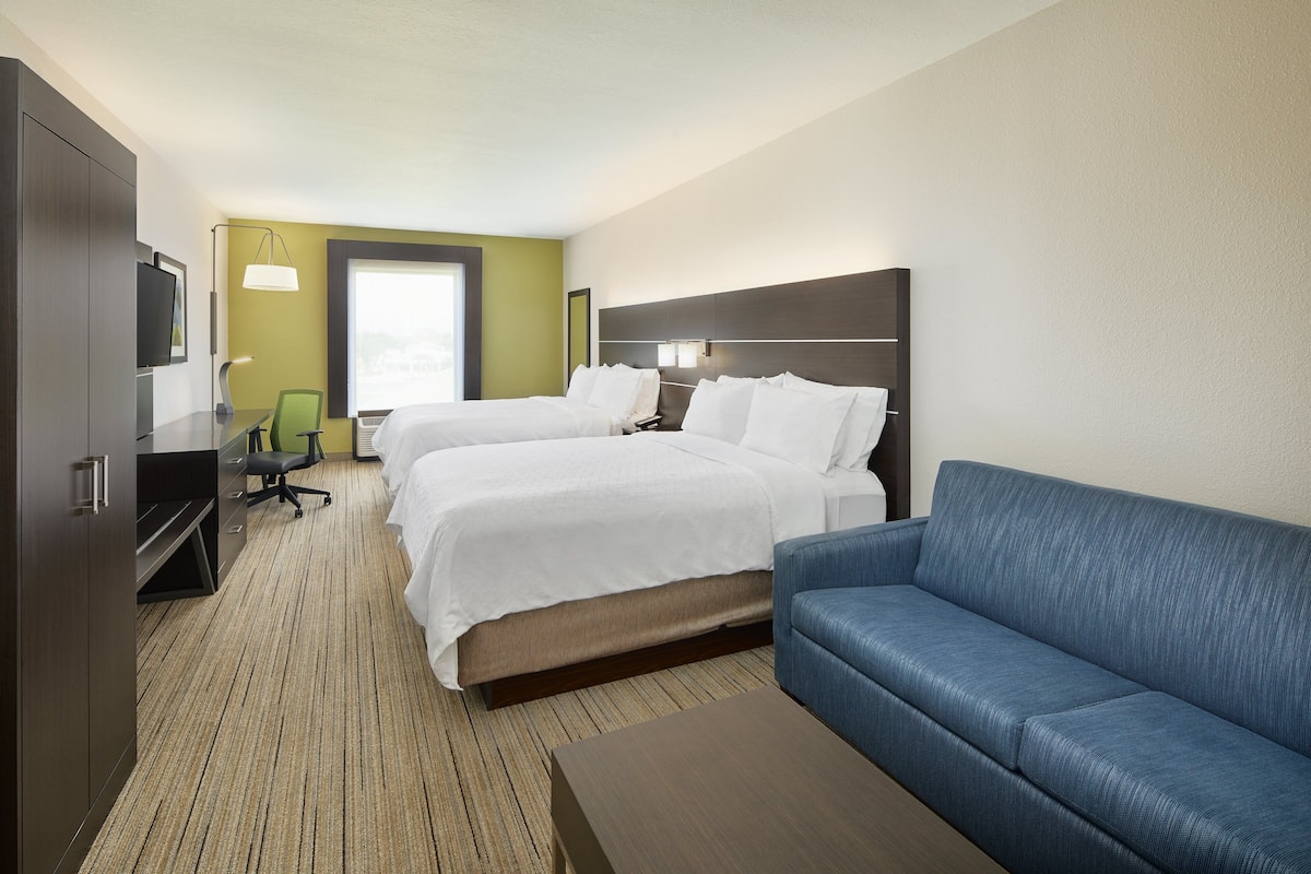 A hotel room with two beds, a sofa, a desk, and a TV.