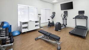 A gym with exercise equipment, a bench, a treadmill, and a wall-mounted TV.