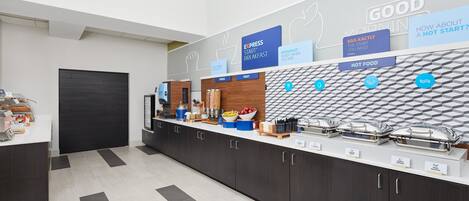 Une cuisine moderne dotée d’un bar pour prendre le petit-déjeuner, où sont indiqués les différents aliments proposés, comme des céréales, des fruits et des plats chauds.
