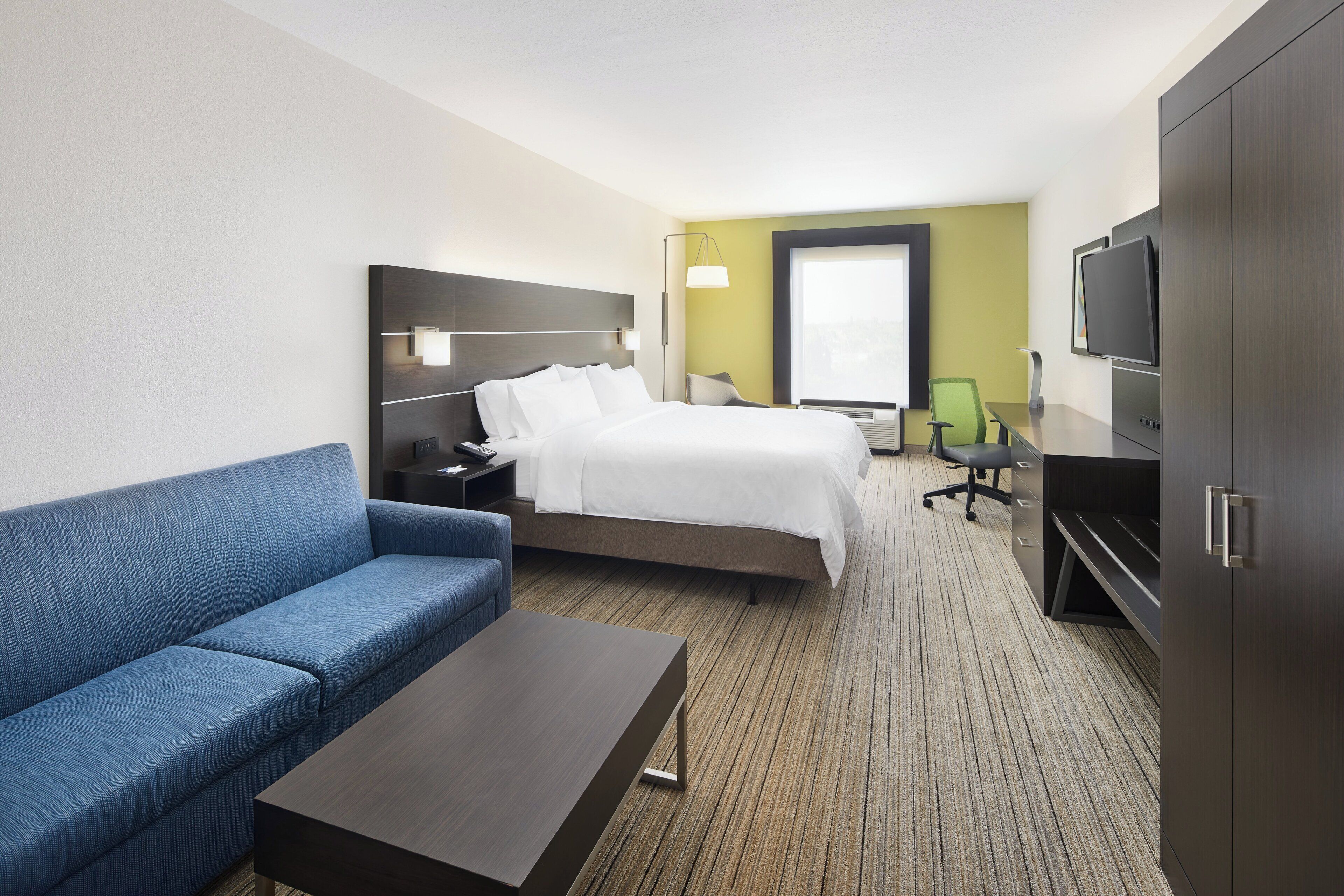 Ein Hotelzimmer mit einem Bett, einem blauen Sofa, einem kleinen Tisch, einem Fernseher und einem Schreibtisch mit Stuhl.