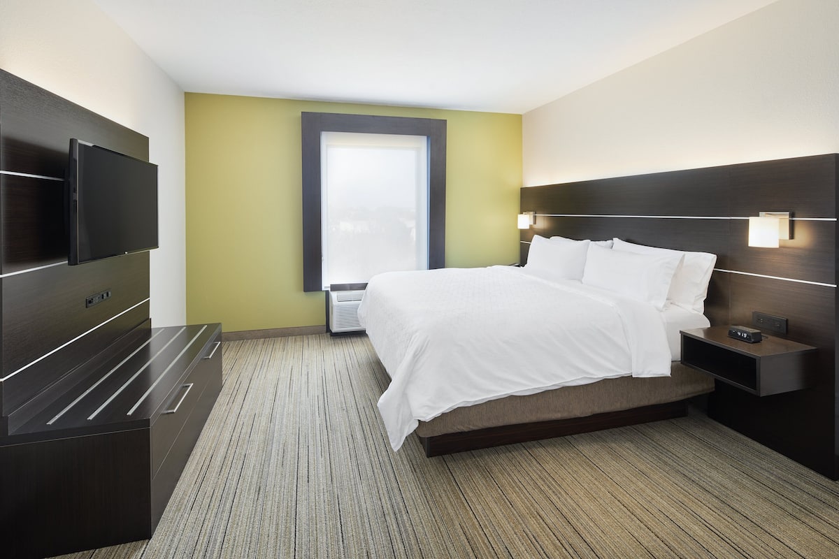 A hotel room with a bed, bedside tables, a flat-screen TV, a window, and a wall-mounted lamp.