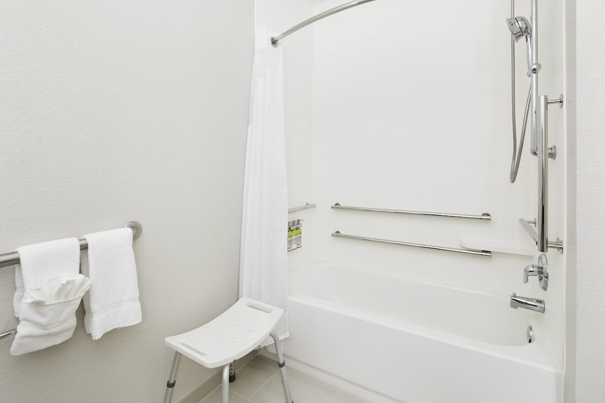 A modern bathroom with a walk-in shower, grab bars, and a white towel rack.