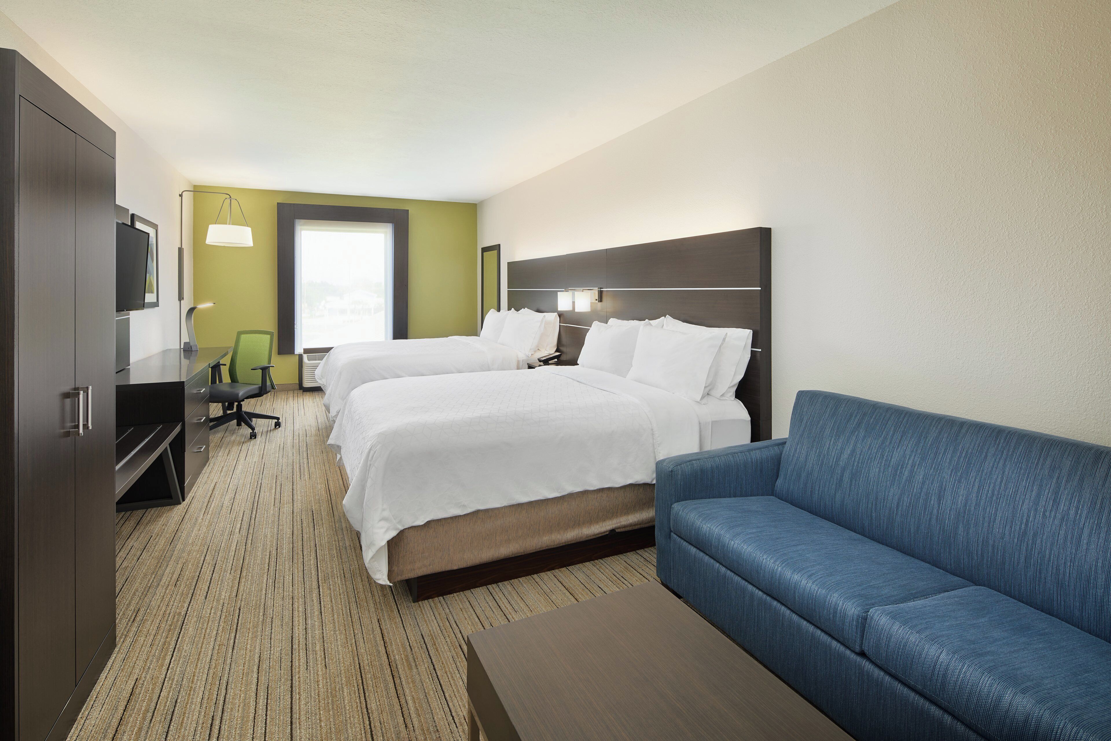 Ein Hotelzimmer mit zwei Betten, einem Sofa, einem Schreibtisch und einem Fernseher.