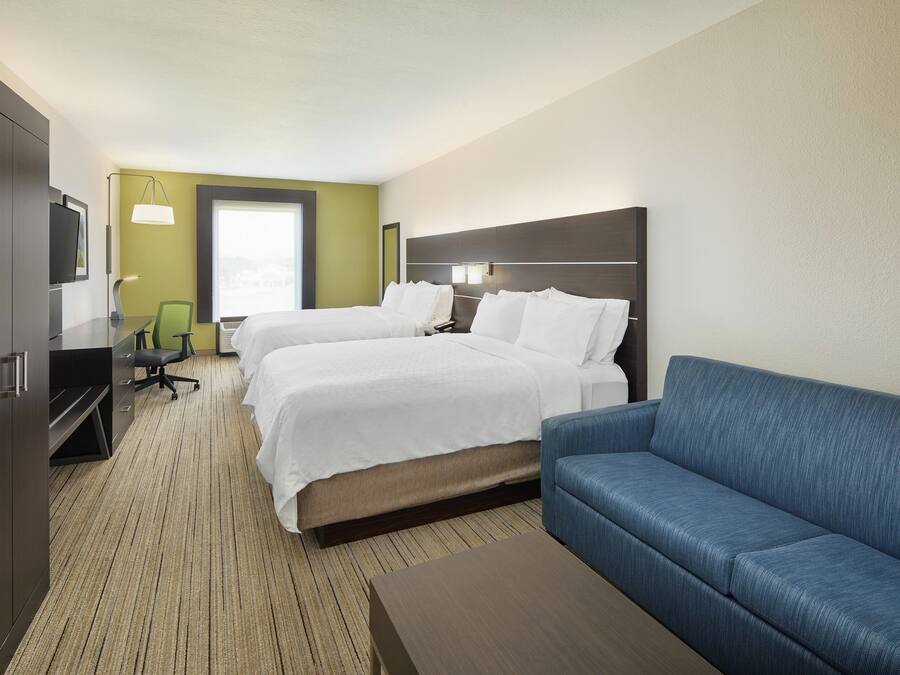 A hotel room with two beds, a sofa, a desk, and a television.