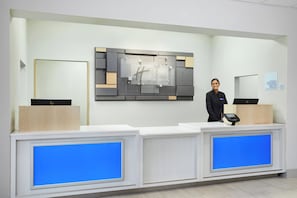 Una recepción de hotel con diseño moderno, un espejo grande y un quiosco digital para el registro.