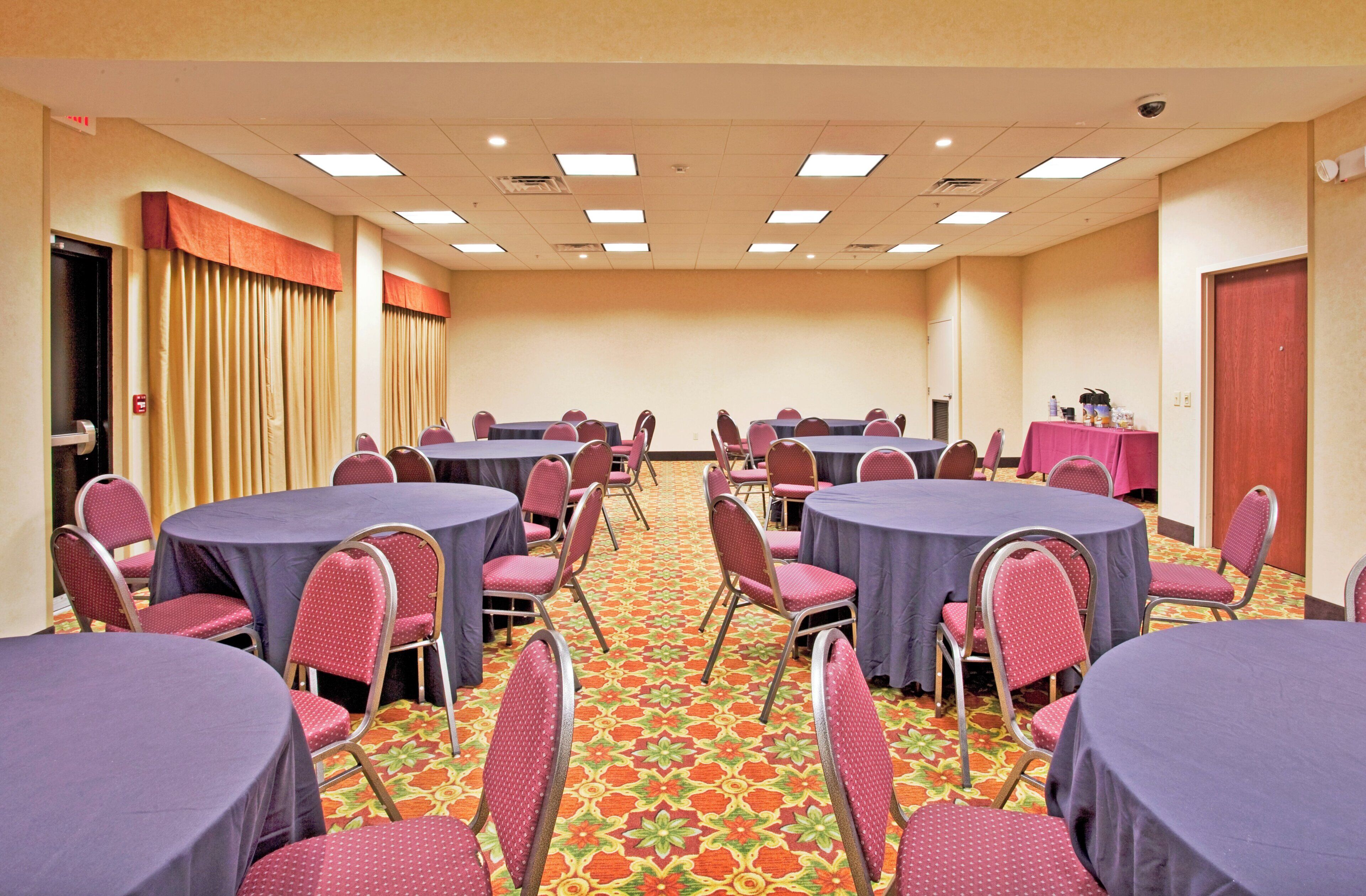 Un salón de conferencias con mesas y sillas redondas, piso alfombrado y una puerta a la izquierda.
