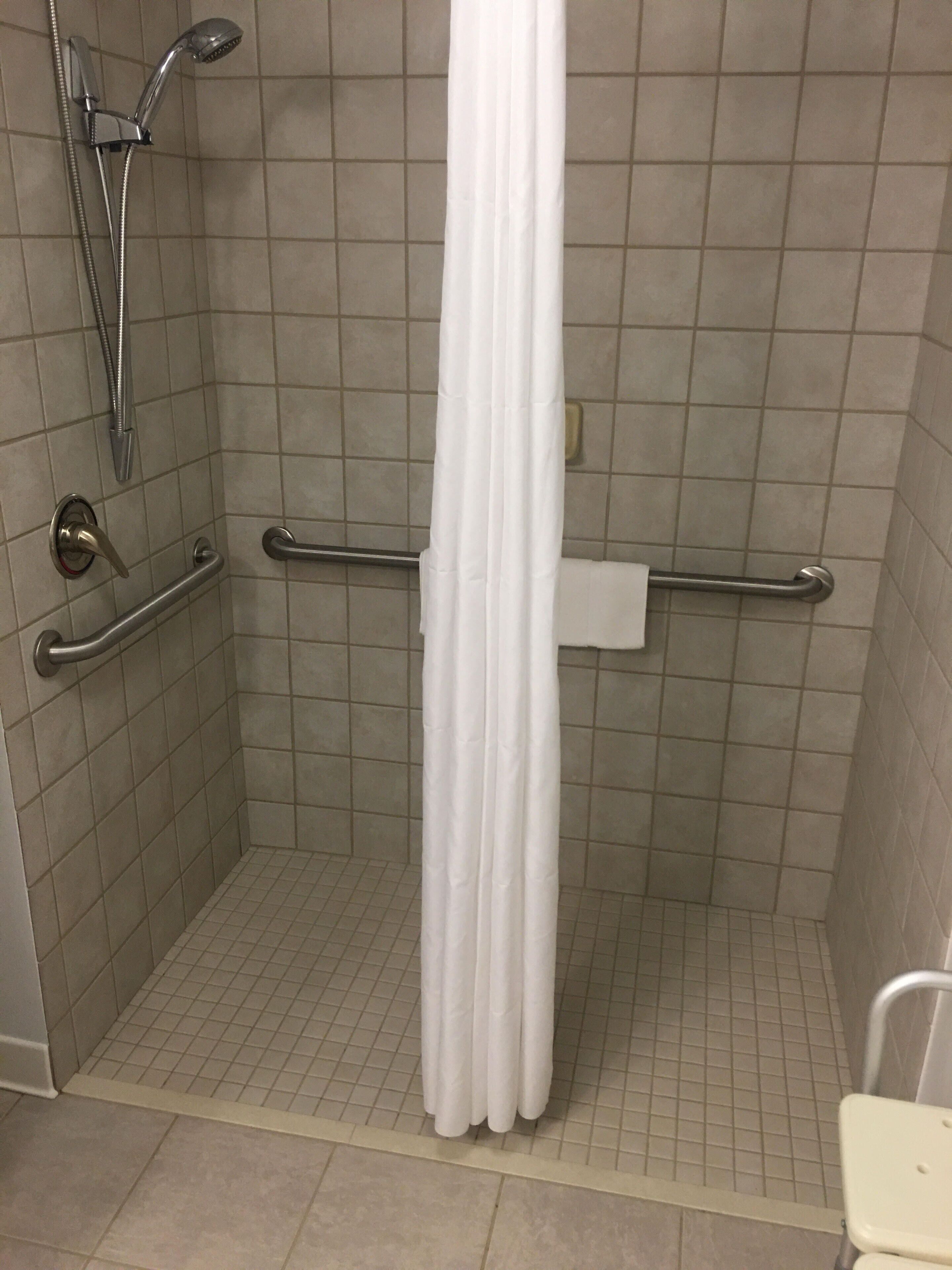 Eine Duschkabine mit weißer Duschvorhang, Haltegriffen und einer Handbrause.