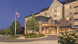 A Country Inn & Suites by Radisson building with a covered entrance, flag, and landscaped area. - Country Inn & Suites by Radisson, Grand Rapids East, MI (Grand Rapids)