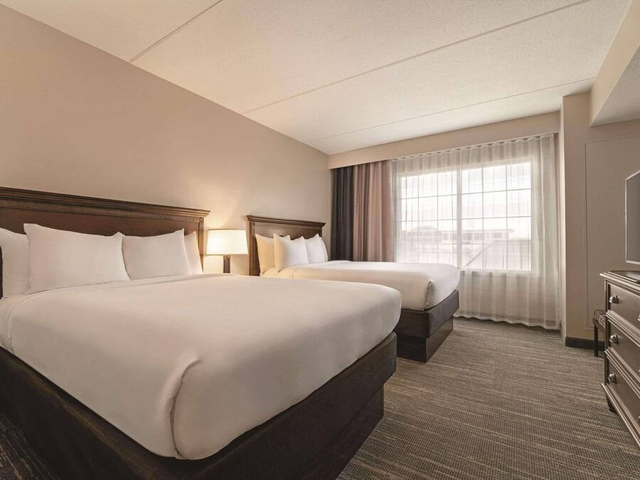 A hotel room with two beds, a TV, a dresser, and a window with curtains.